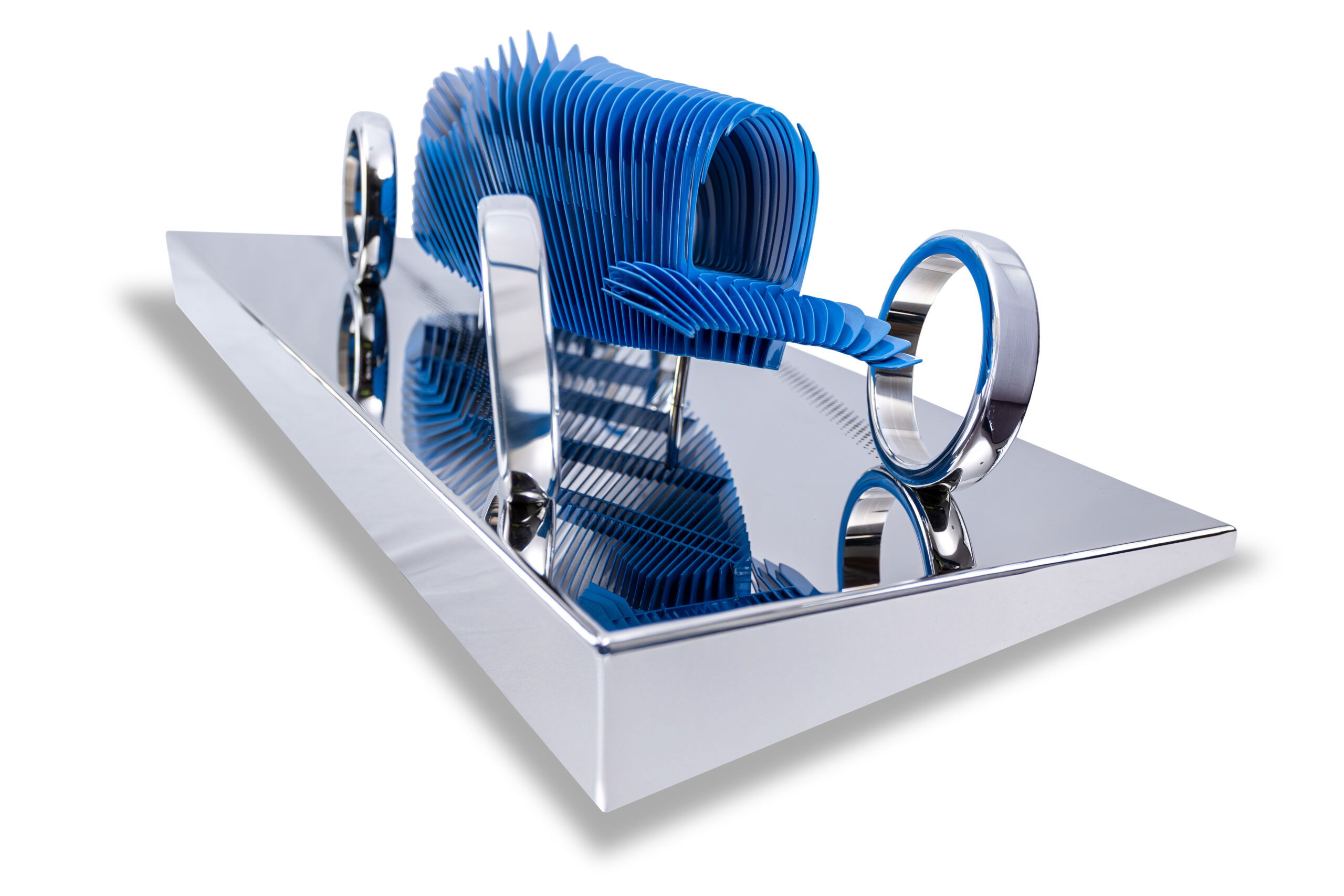 Antoine Dufilho – Bugatti 35 Blue De Bugatti 35 Blue van Antoine Dufilho is een moderne interpretatie van een icoon uit de autogeschiedenis. Dit sculptuur laat zien hoe traditie en innovatie elkaar versterken. Door het gebruik van metalen lagen, zorgvuldig geplaatst en ritmisch opgebouwd, krijgt de Bugatti een abstracte en toch herkenbare vorm. De blauwe kleur is een ode aan het Franse race-erfgoed. Tegelijkertijd benadrukt het werk de pure elegantie van de Bugatti 35, een van de meest legendarische racewagens ooit gebouwd. De reflecterende basis versterkt de diepte van de sculptuur en speelt met licht en perspectief. Daardoor lijkt de auto voortdurend in beweging, alsof hij klaarstaat om snelheid te maken. Dufilho’s aanpak is zowel architectonisch als artistiek. Elke laag is met precisie ontworpen en draagt bij aan de balans tussen leegte en massa. Zo ontstaat een harmonie die zowel kracht als verfijning uitstraalt. De Bugatti 35 Blue is niet alleen een eerbetoon aan autodesign, maar ook een experiment met vorm, ruimte en illusie. Het kunstwerk nodigt de toeschouwer uit om vanuit verschillende hoeken te kijken. Vanuit elke positie ontdek je nieuwe lijnen, schaduwen en ritmes. Daardoor blijft de sculptuur verrassen en inspireren. Bovendien benadrukt dit de visie van Dufilho: kunst moet dynamisch zijn en een dialoog aangaan met zijn omgeving.