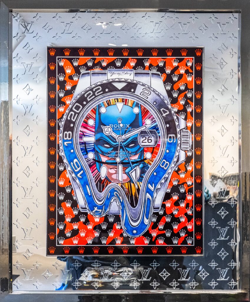 Rolex Batman Laser Cut - Yaniv Edery Rolex Batman Laser Cut is an explosion of luxury, power and symbolism. The artwork depicts a distorted Rolex GMT-Master combined with iconic patterns from Louis Vuitton. This fusion of horology and high fashion creates a breathtaking visual spectacle. Moreover, the precision of the laser cut makes the work impressively modern. The bright blue hues contrast sharply with the fiery red and black, making the energy of the canvas immediately palpable. The Rolex in the center seems to melt, like a reference to time warping. This reinforces the message: luxury is not just possession, but experience. The interplay of symmetry and chaos makes the work intriguing. Each glance reveals new details, each line highlights craftsmanship. Therefore, Rolex Batman Laser Cut is more than a work of art; it is a statement about time, power and identity. The reflective frame, featuring the Louis Vuitton pattern, heightens the sense of exclusivity. The work exudes sophistication, but also challenges. Because on the one hand it displays luxury, on the other hand it breaks open this tradition through distortion. This creates a powerful dialogue between tradition and innovation. This masterpiece is ideal for collectors who dare to choose. It combines modern design, iconic brands and artistic freedom. With powerful colors, sharp lines and striking details, it always attracts attention.