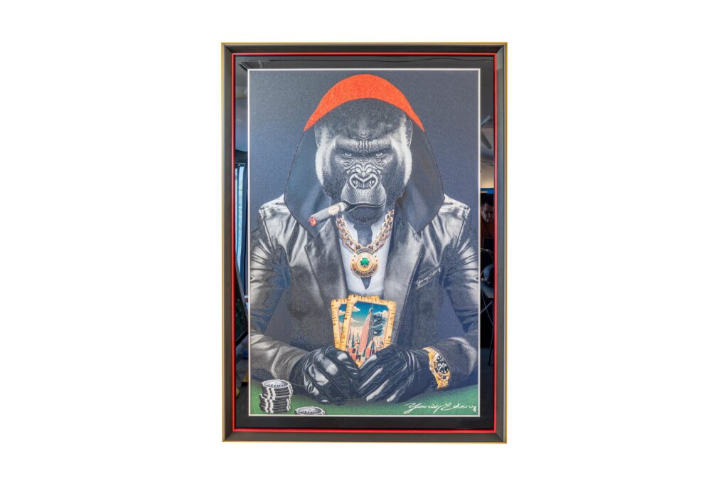 Yaniv Edery - Gorilla Poker Cape Red is a powerful work of art that brings together dominance, luxury and style. The imposing gorilla sits at the poker table, clad in a tough leather jacket and a bright red cape. The details draw immediate attention: a large gold chain, striking rings and a cigar symbolizing power and authority. The red cape is not only a stylish detail, but also a symbol of power and leadership. It makes the gorilla a true ruler of the game. Thereby, the bright contrasts and deep colors enhance the intensity of the work. The gorilla's gaze is determined and unyielding. He radiates that he is in control of the cards and thus of the whole situation. The poker theme adds another layer to the artwork. Poker is all about risk, strategy and daring. Exactly these elements Edery manages to translate into his art. The cards, the chips and the pose of the gorilla bring together tension and elegance. The work feels both playful and impressive at the same time, a combination that continues to fascinate. Every detail in this work is carefully chosen. From the shine on the jewelry to the sharp contours of the gorilla's face, everything exudes luxury and power. This makes the artwork not only a visual highlight, but also a story about power, guts and identity. Gorilla Poker Cape Red is an eye-catcher that completely transforms a space. It exudes energy, confidence and character, inviting conversation and admiration.